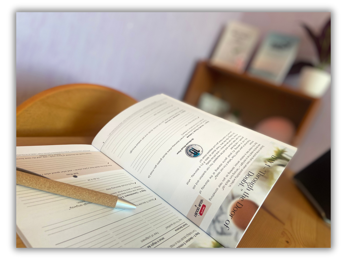 Open pages of the Delete Your Doubt physical journal with a pen